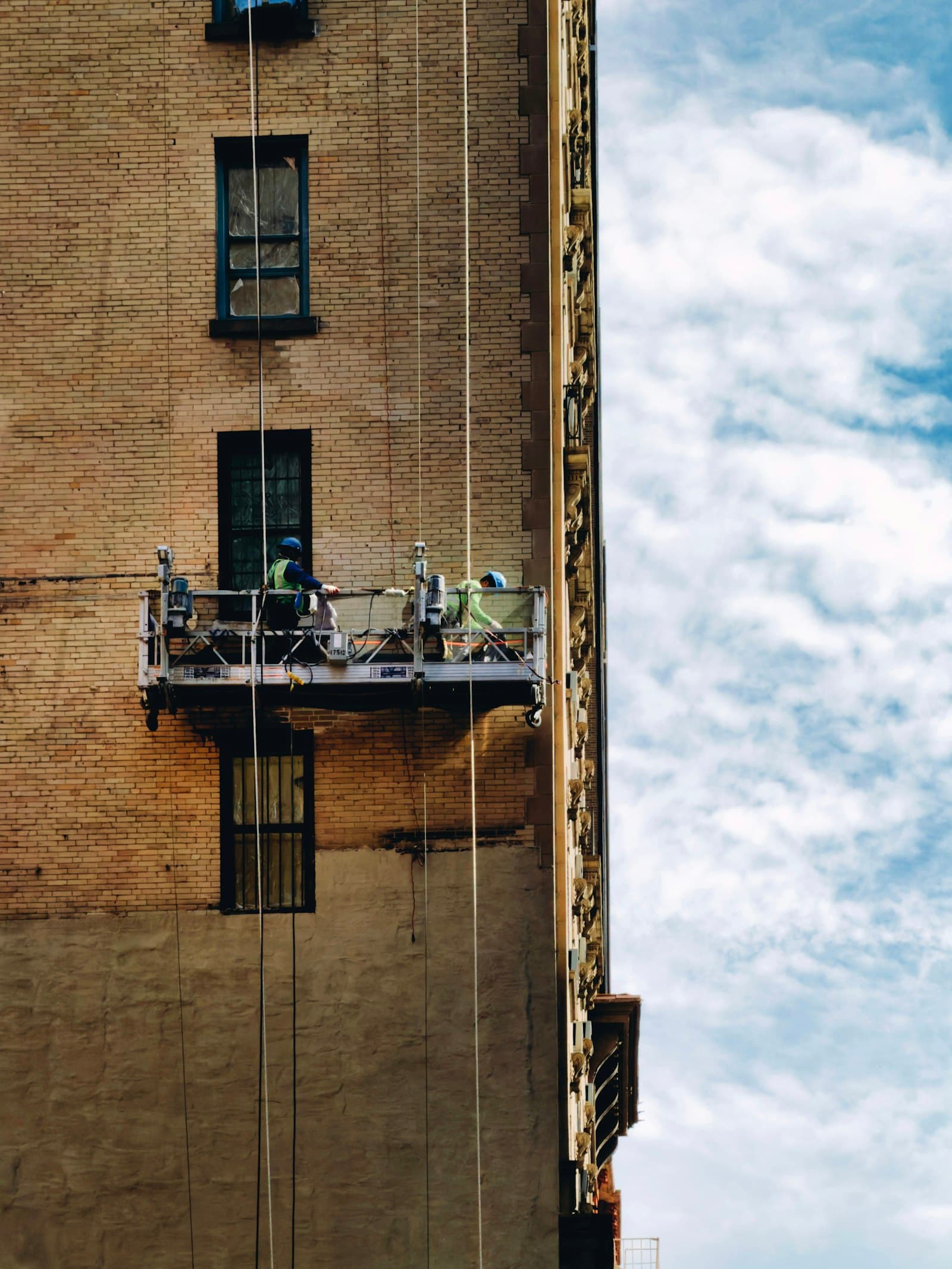 Workers on a suspended platform finishing a building's facade.